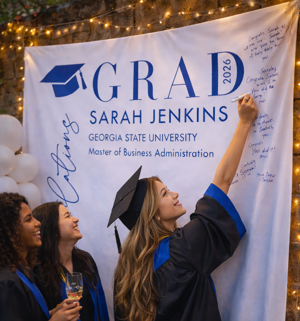 Graduates in caps and gowns signing a 'GRAD 2026' banner at Georgia State University.