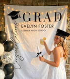 Graduating high school senior holding a drink in front of a 'GRAD' banner with personalized details.