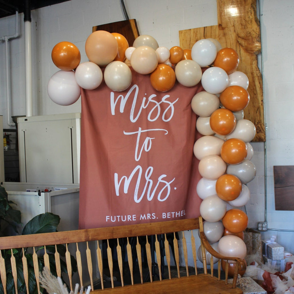Decorative arch with balloons and a banner reading 'Miss to Mrs.' in a room.